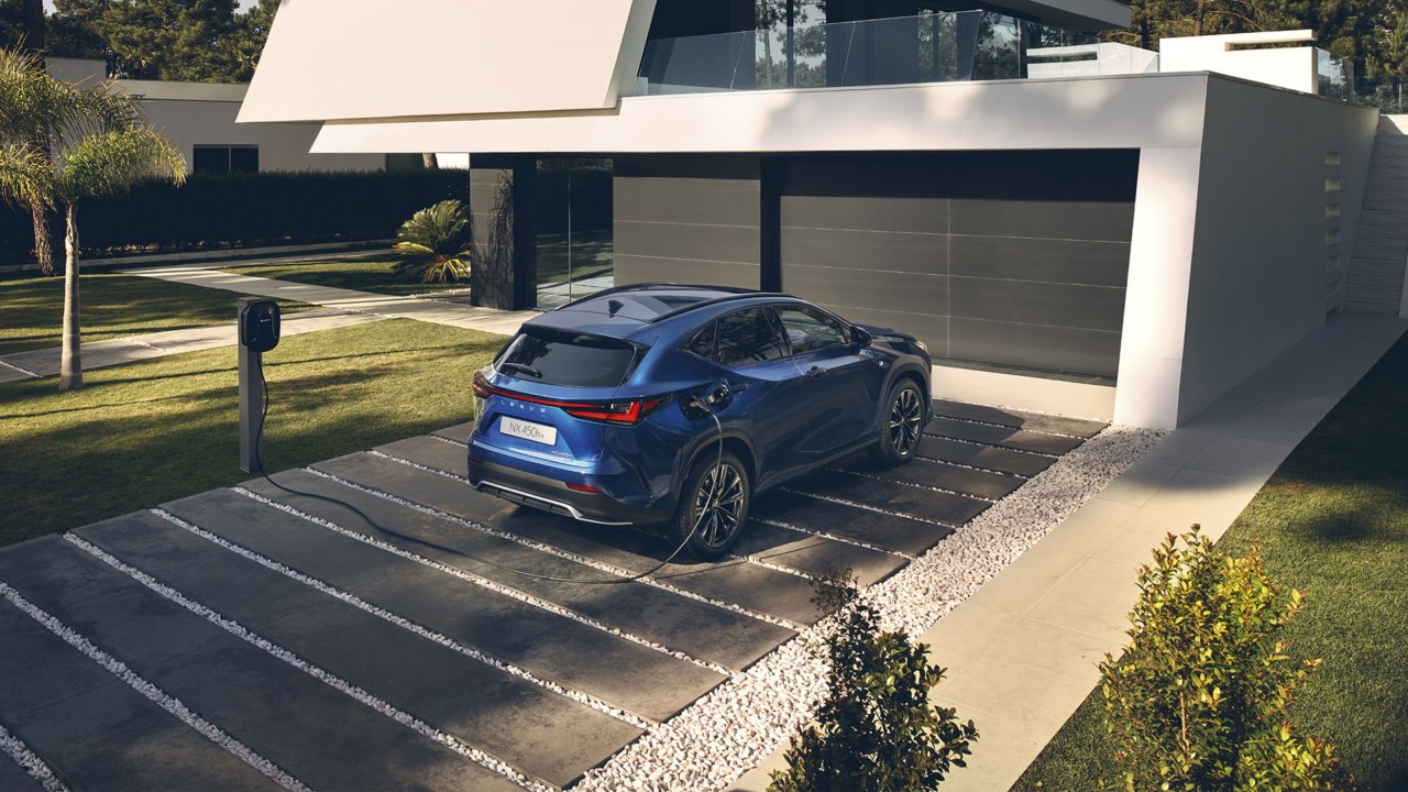 A Lexus NX 450h+ plugged into a charging station outside a home